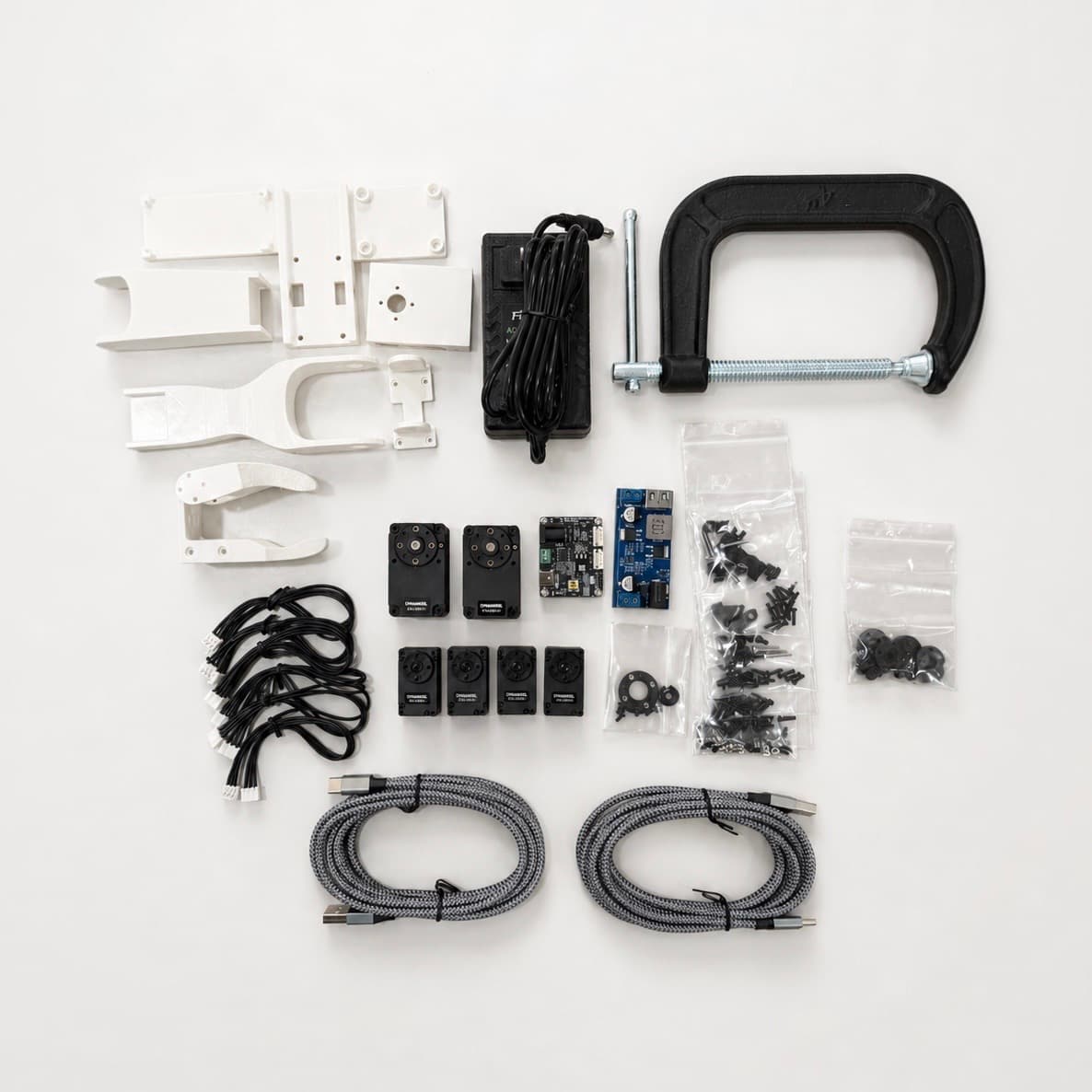 Robotic arm parts, servos, cables, hardware, and tools arranged before assembly.